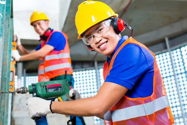 Een mbo-student in werkkleding met veiligheidshelm aan het werk met een boormachine