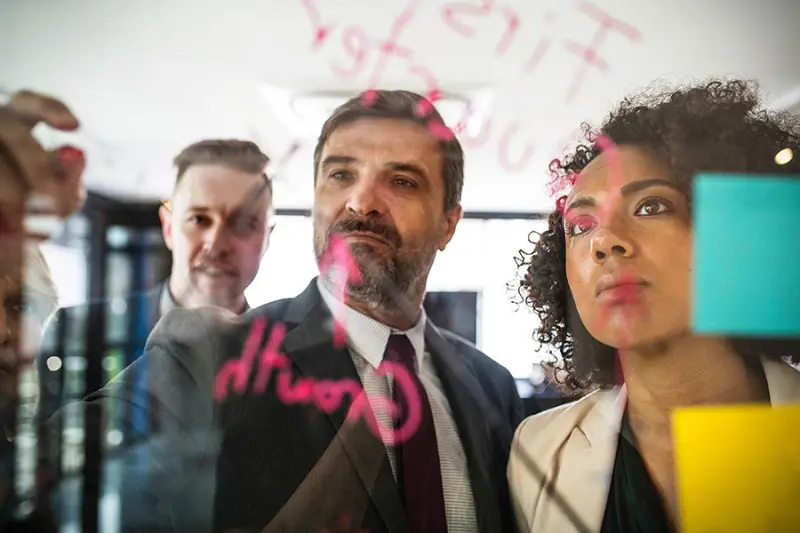 Een managementteam brainstormt met post-its op een glazen wand